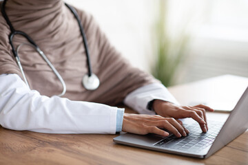 Cropped of female doctor using laptop, sitting in her cabinet - obrazy, fototapety, plakaty