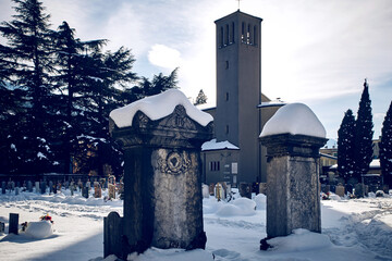 Snowy italian cemetery with two old big graves against the background of the church