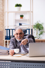 Old male employee drinking coffee in the office