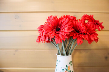 red colorful gerbera flowers in a vase on the wooden wall background