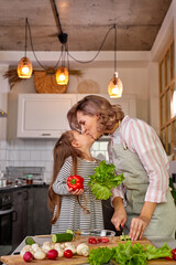 friendly parent mom kissing with cute child girl while cooking together, making salad