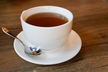 white cup of tea on plate with teaspoon on wooden table in cafe