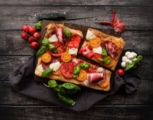 Italian rectangular pizza with tomatoes, mozzarella and briazolla on a wooden table. The view from the top - 403075818