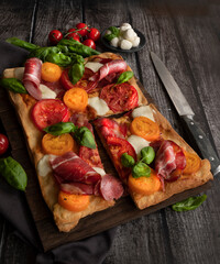 Italian rectangular pizza with tomatoes, mozzarella and briazolla on a wooden table.