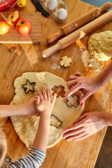 girl baking cookies with mum, rolls out the dough and uses moulds to make the cookie cuttings. top view