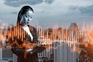 Attractive Asian trader in suit examine her notes to predict the market behavior based on historic data and stock market. Corporate finance fund and forex chart. Singapore. Double exposure.