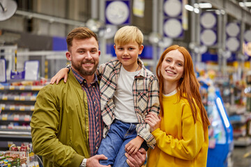 family enjoy shopping with child boy, young parents in supermarket aisle with cute kid boy, in casual wear, smile