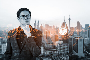 A young handsome eastern cybersecurity developer thinking about new concepts at security compliance division to protect clients confidential information. IT lock icons over Kuala Lumpur background.
