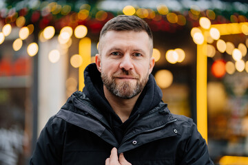 a middle-aged man with a beard on a winter street against of festive lights