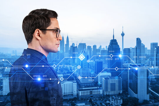 Eastern young businessman pondering on technology at business process to achieve tremendous growth. Worldwide process to conduct transactions. Tech hologram icons over Kuala Lumpur background
