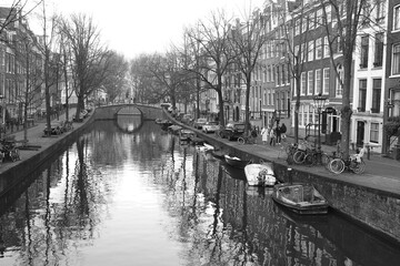 Fototapeta premium Amsterdam Canal View with Bridge, Winter Trees, Boats and Reflections in Black and White