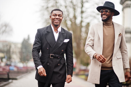 Two fashion black men walking on street. Fashionable portrait of african american male models. Wear suit, coat and hat.