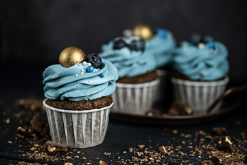 Several muffins or cupcakes with blue shaped cream and with blueberrieson at black table against a...