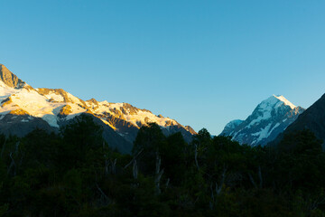 Sun at sunrise strikes snow-capped mountian peaks beyond silhouette of foreground hills of Southern Alps, Canterbury New Zealand.