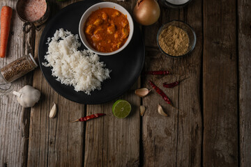 Plate with delicious chicken curry and rice on rustic wooden table with spices background. Traditional Indian dish. Exotic tasty meal. Appetizing photo for menu or cookbook. View from above.