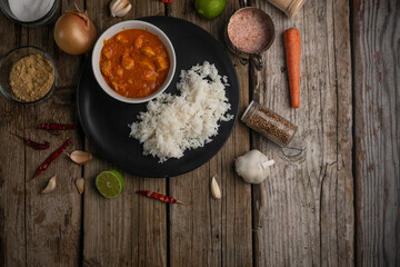 Plate with delicious chicken curry and rice on rustic wooden table with spices background. Traditional Indian dish. Street meal. Appetizing photo for menu or cookbook. Space for text. Top view.