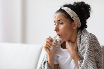 Woman covered in blanket coughing, home interior