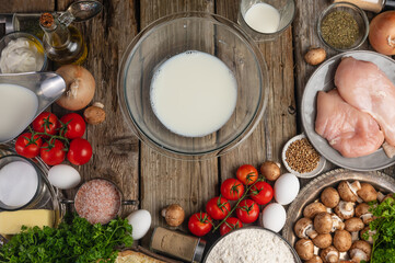 The glass bowl with milk for preparing dough on variety of ingredients background. Concept of cooking process. Backstage of preparing meat pie. View from above.