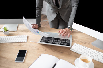 partial view of trader holding infographics near laptop, monitors and smartphone with blank screen