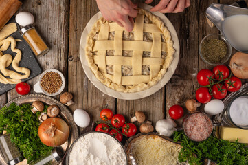 Chefs hands prepares raw pie for baking on variety of ingredients background. Concept of cooking process. Backstage of preparing meat pie. View from above. Frozen motion.