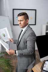 Naklejka premium thoughtful trader in formal wear holding infographics in office