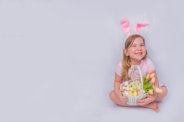 Obraz na płótnie Canvas Happy cute girl with bunny ears. Easter greeting card background. with Easter eggs and spring flower in basket