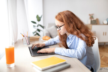 Girl sitting at table, using laptop, typing on keyboard