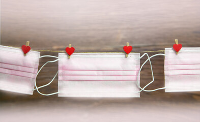 Pink protective medical mask hanging with clothes pegs in heart shape isolated on white background,...