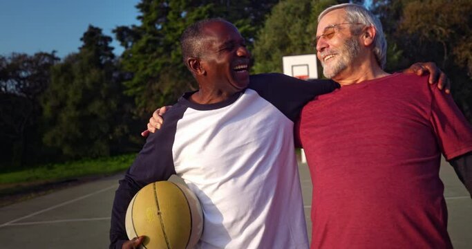 African-american senior man embracing friend holding basketball on outdoors court