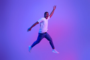 Excited Funny Black Guy Jumping Up In Neon Light Over Purple Background