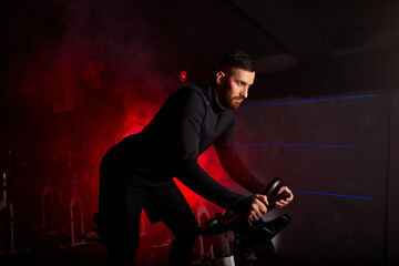 Fototapeta na wymiar sportsman is exercising in class in fitness center, in red neon lighted smoky space, in black sportive outfit, has intensive training