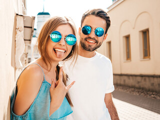Portrait of smiling beautiful woman and her handsome boyfriend. Model in casual summer jeans dress. Happy cheerful family. Female having fun. Couple posing on the street background in sunglasses