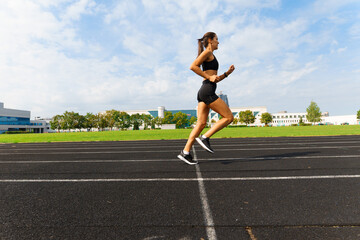 Fototapeta na wymiar Outdoor shot of young woman athlete running on racetrack. Professional sportswoman during training.