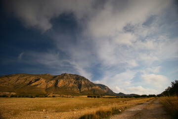 Camino rural. Valle y montaña al final del verano con pasto seco. Cielo con cirros o nubes altas. Sierra del Buey, Jumilla (Murcia).