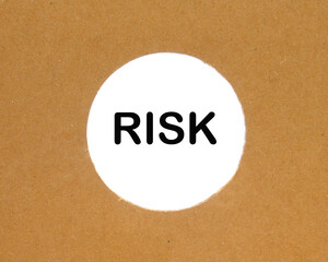 The text Risk behind torn brown paper. cut out round hole in cardboard on white background