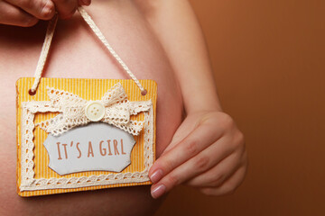 A pregnant woman holds a sign It is a girl  next to her belly on a yellow background