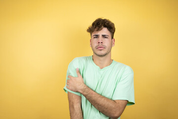 Handsome man wearing a green casual t-shirt over yellow background with pain on his shoulder and a painful expression