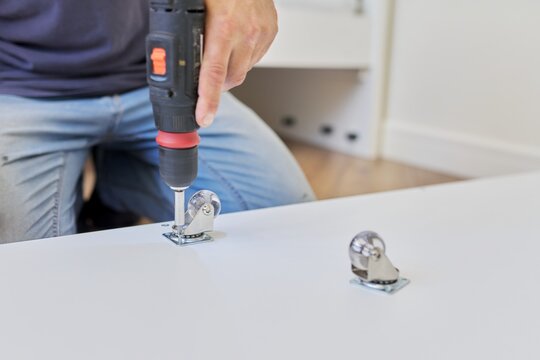 Furniture wheels close-up. Worker hands assembling furniture using professional tool