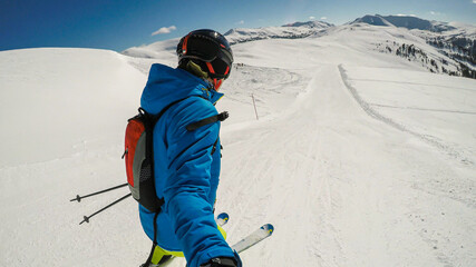 A skiing man in colorful outfit taking a selfie while going down the ski run in Innerkrems,...
