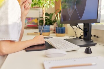 Close-up of young woman's hand drawing on computer using graphics tablet