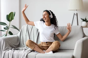 Foto op Canvas Carefree woman listening to music and singing, using headphones © Prostock-studio
