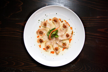 Sashimi of fresh sea bream in thin slices and olive oil served on a white plate on black wooden...