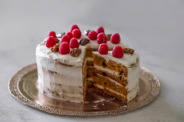 Close up carrot cake decorated with raspberry and pecan nuts stock photo. Sliced homemade carrot cake on light bckground