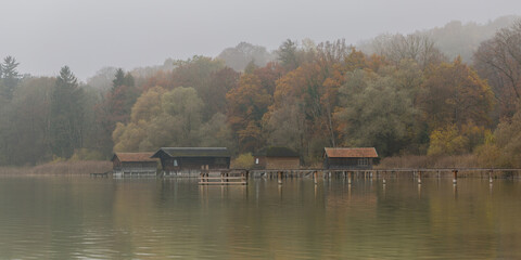 Fototapeta premium View on boathouses at Ammersee lake. Idyllic bavarian landscape on a foggy autumn day.