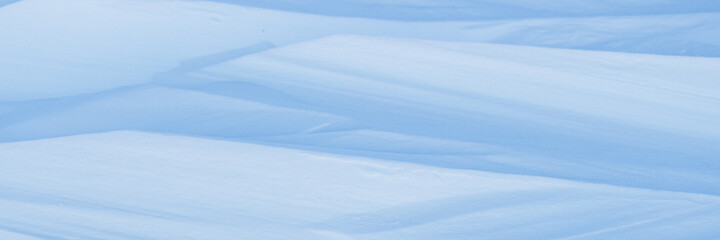 Beautiful winter background with snowy ground. Natural snow texture. Wind sculpted patterns on snow surface. Wide panoramic texture for background and design.