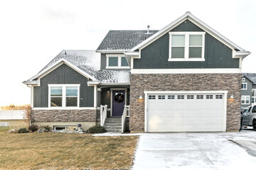 A modern dark gray and white new construction craftsman with stone accents and a purple front door...