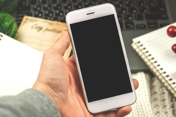 Business concept on winter cozy holiday, man holding black white smartphone on background of decoration