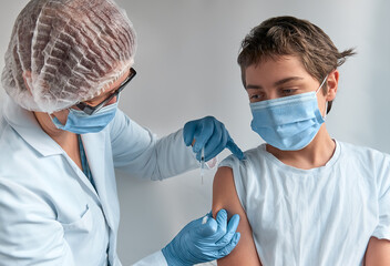 Coronavirus, flu or measles vaccine concept. Medic, doctor or nurse in protective gown and face mask vaccinates teenage boy with vaccine in syringe.