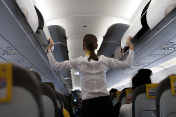 Passenger plane interior with a female flight attendant closing overhead