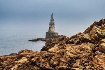 rocks and sea and the lighthouse in the fog